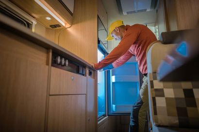Un camper parcheggiato in riva a un lago sotto un cielo azzurro brillante con nuvole, sedie e un frigo portatile all'esterno.