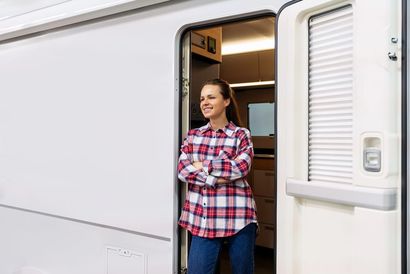 Donna in piedi sulla soglia di un camper, con le braccia incrociate e una camicia a quadri rossa.