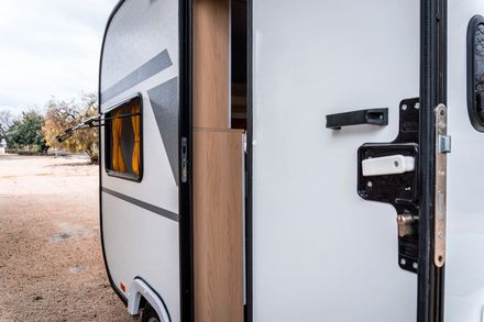 Apri la porta di un camper bianco con finiture in legno in un campeggio