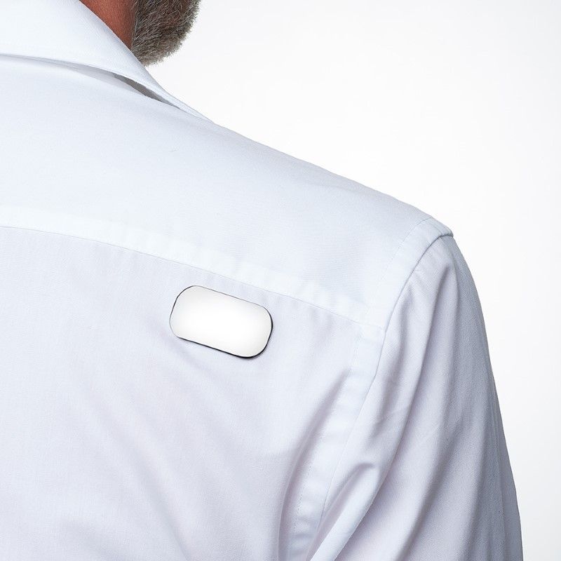Witte overhemdschouder met een rechthoekig, zilverkleurig voorwerp eraan bevestigd. Energetix Body Magnet