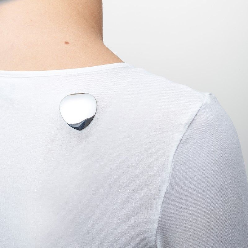 Persoon met een wit shirt met een zilverkleurig, hartvormig voorwerp op de rug. Energetix Body Magnet