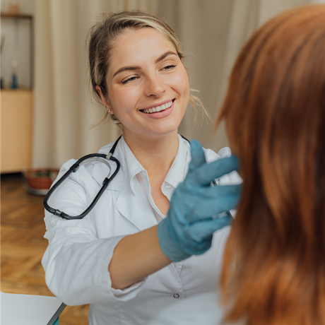 Doctor examining a patient's mouth with a gloved hand; stethoscope around her neck.