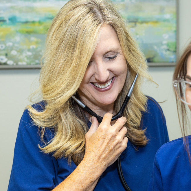 Woman in medical scrubs discusses notes with a patient in a light-filled office.