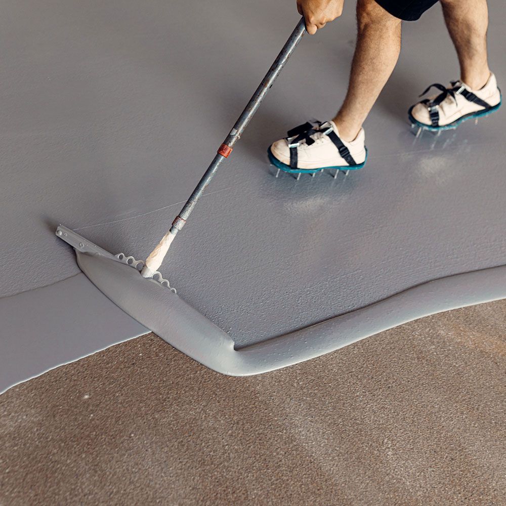 A person is using a rake to spread paint on the floor A person is using a rake to spread paint on the floor