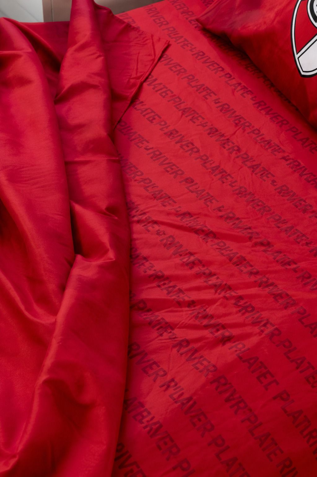 Cama roja con motivos del Liverpool y almohada a juego en un acogedor dormitorio beige.