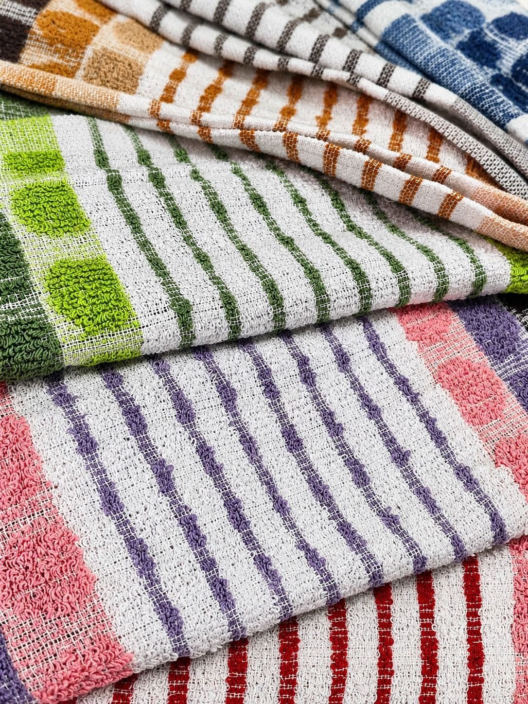 Pila de paños de cocina coloridos y estampados sobre la encimera de la cocina, junto al fregadero y una maceta.