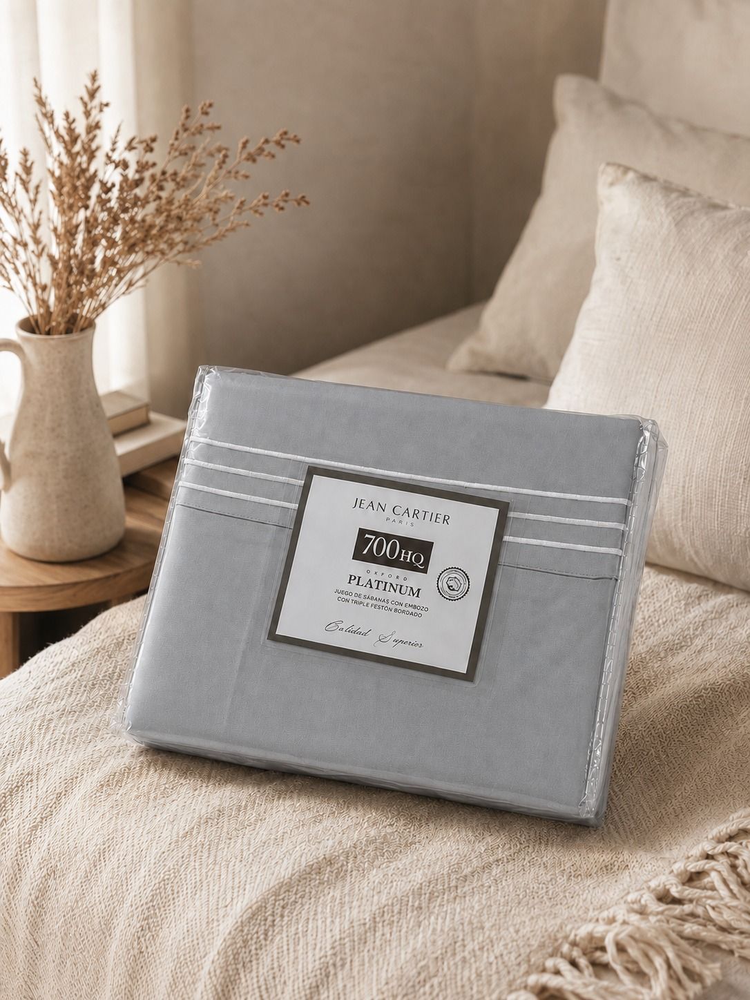 Cama bien hecha con ropa de cama gris claro, almohadas y una cesta de mimbre al lado.