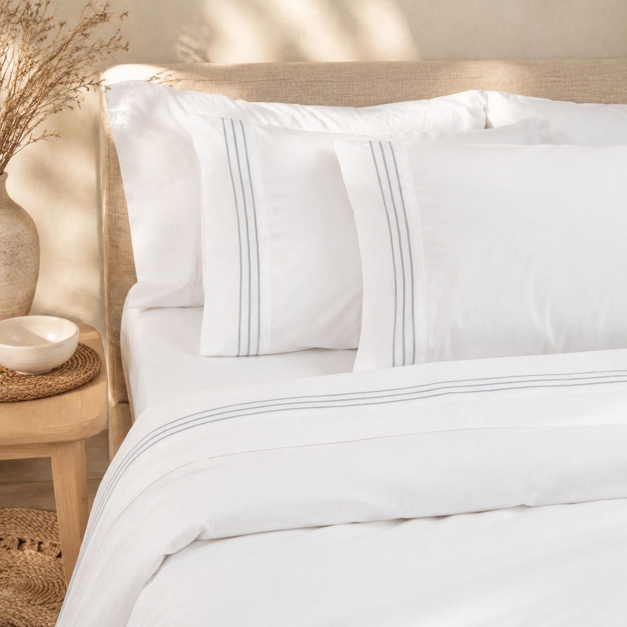 Cama blanca con almohadas y edredón a rayas en un dormitorio de tonos beige suaves.
