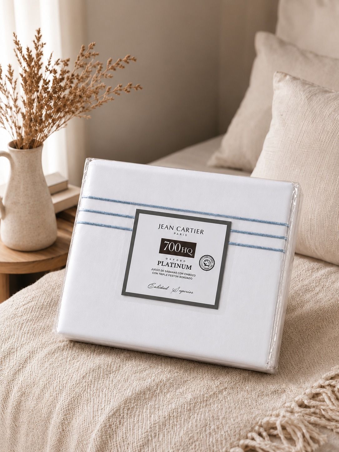 Cama blanca con almohadas y edredón a rayas en un dormitorio de tonos beige suaves.