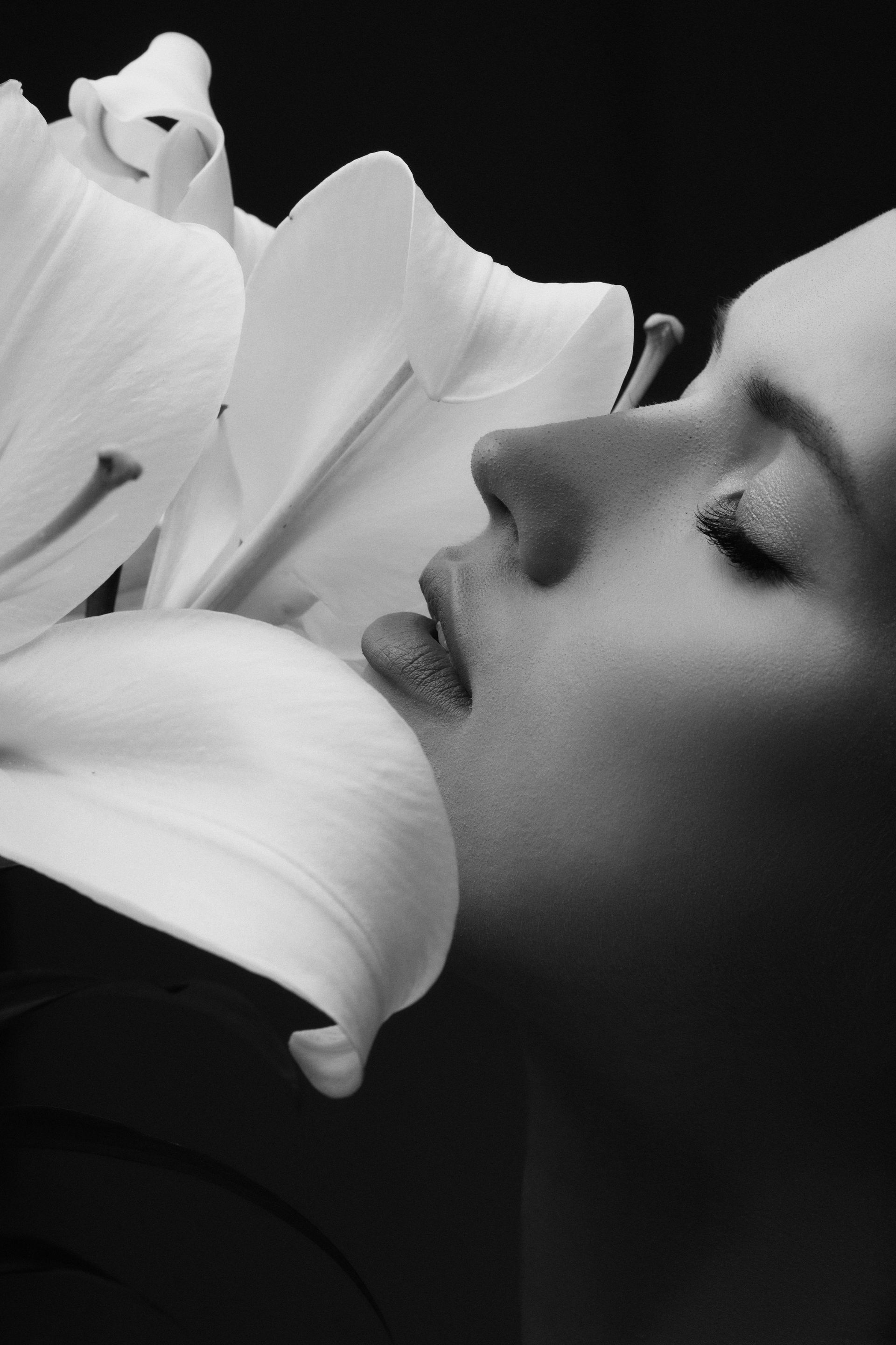Woman's face close to large white lily. Eyes closed, lips touching petals.