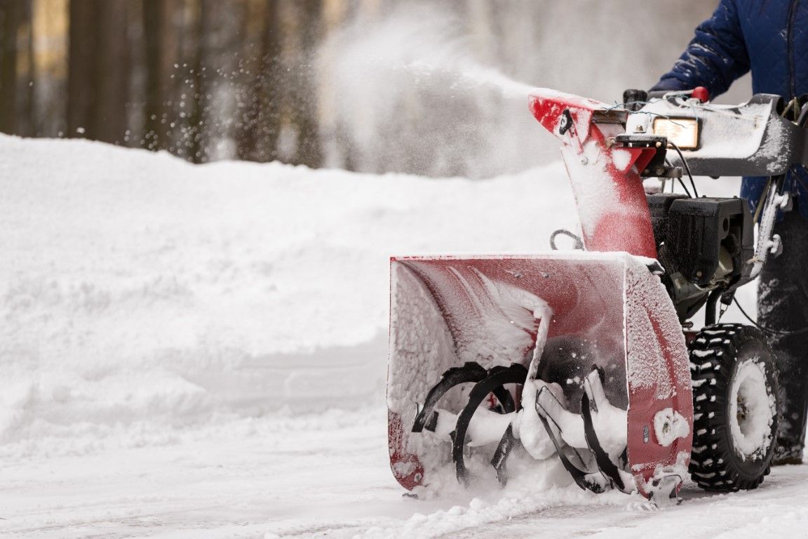 Snowblower clearing a snowy road, red blade pushing snow aside