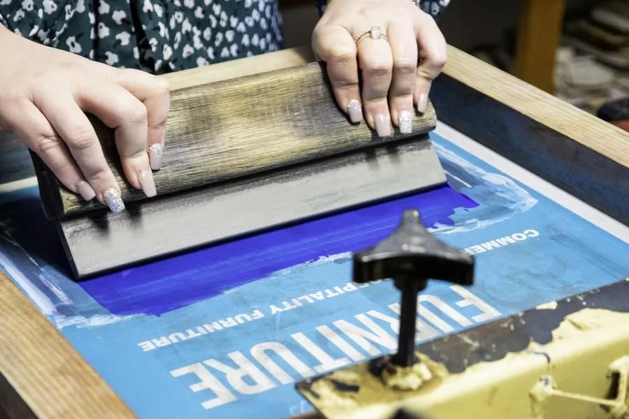 A Person Is Using A Screen Printing Machine To Print A Poster — Sportstar Screenprinting in Dalby, QLD