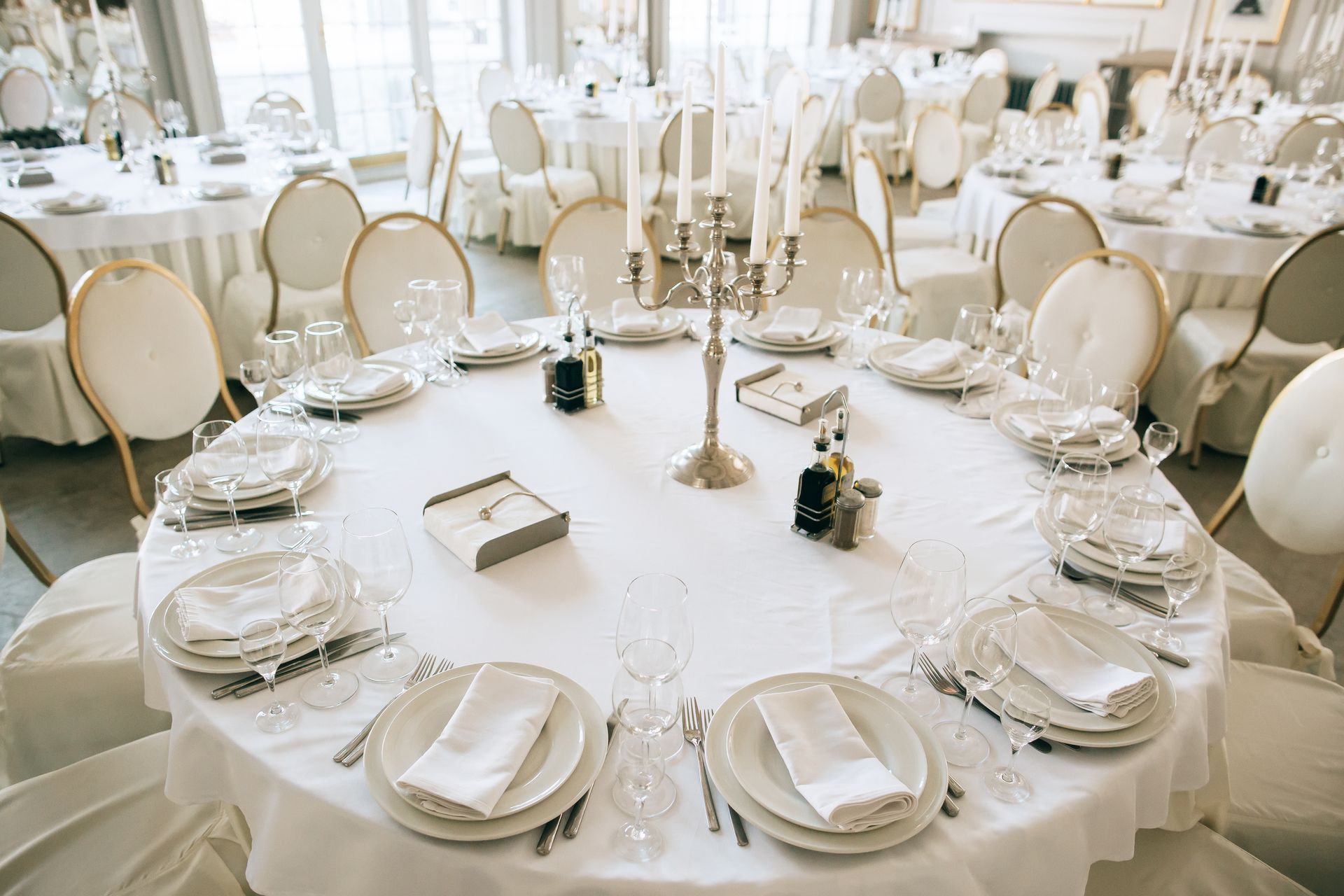 A formal round dining table set for a wedding with white linens, gold-rimmed plates, and a silver candelabra centerpiece.