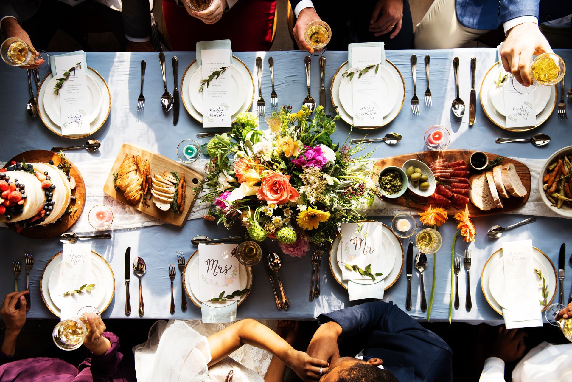 An overhead view of a dinner party table set with plates, floral centerpieces, appetizers, and wine glasses.