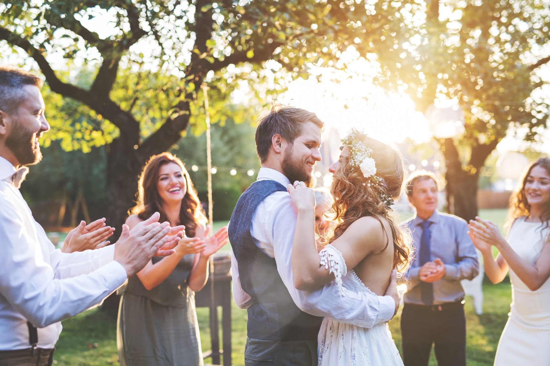 A couple dancing at an outdoor wedding celebration as guests clap for them in the warm, golden sunlight.
