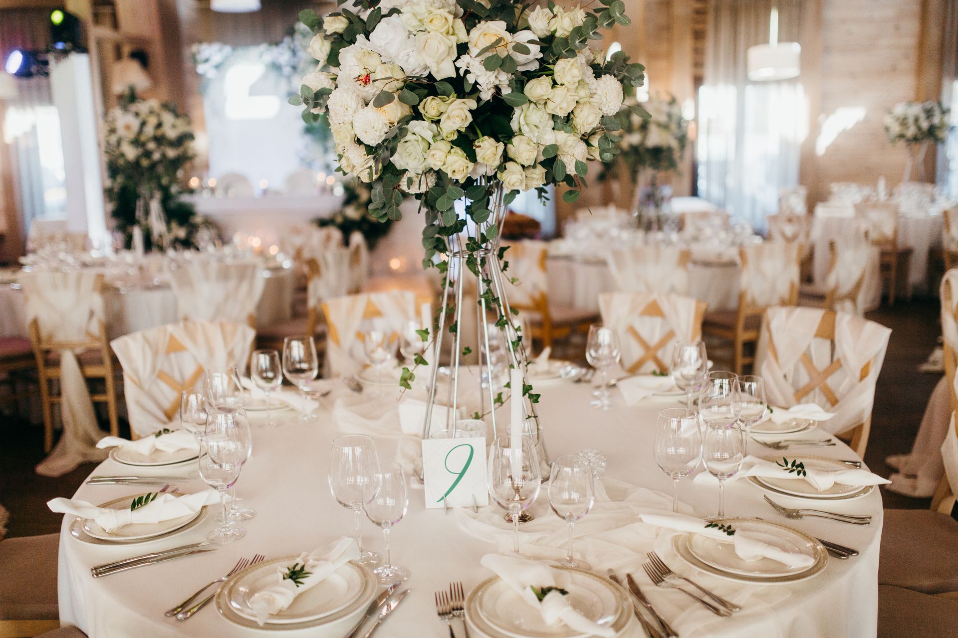 Elegant wedding reception table with a white tablecloth, gold-accented chairs, and a large white floral centerpiece. Elegant wedding reception table with a white tablecloth, gold-accented chairs, and a large white floral centerpiece.