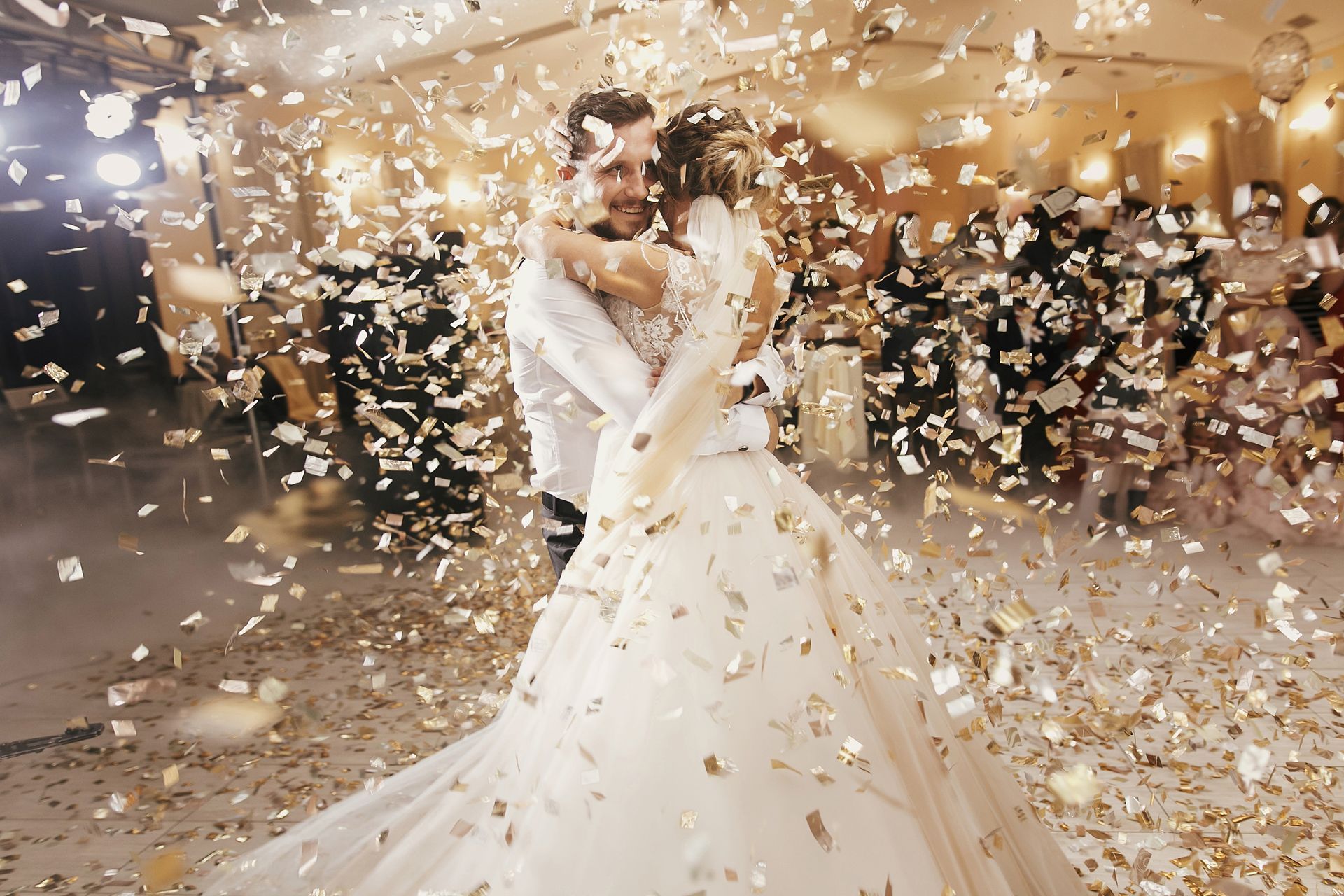 A bride and groom embrace on a dance floor surrounded by falling gold confetti. A bride and groom embrace on a dance floor surrounded by falling gold confetti.