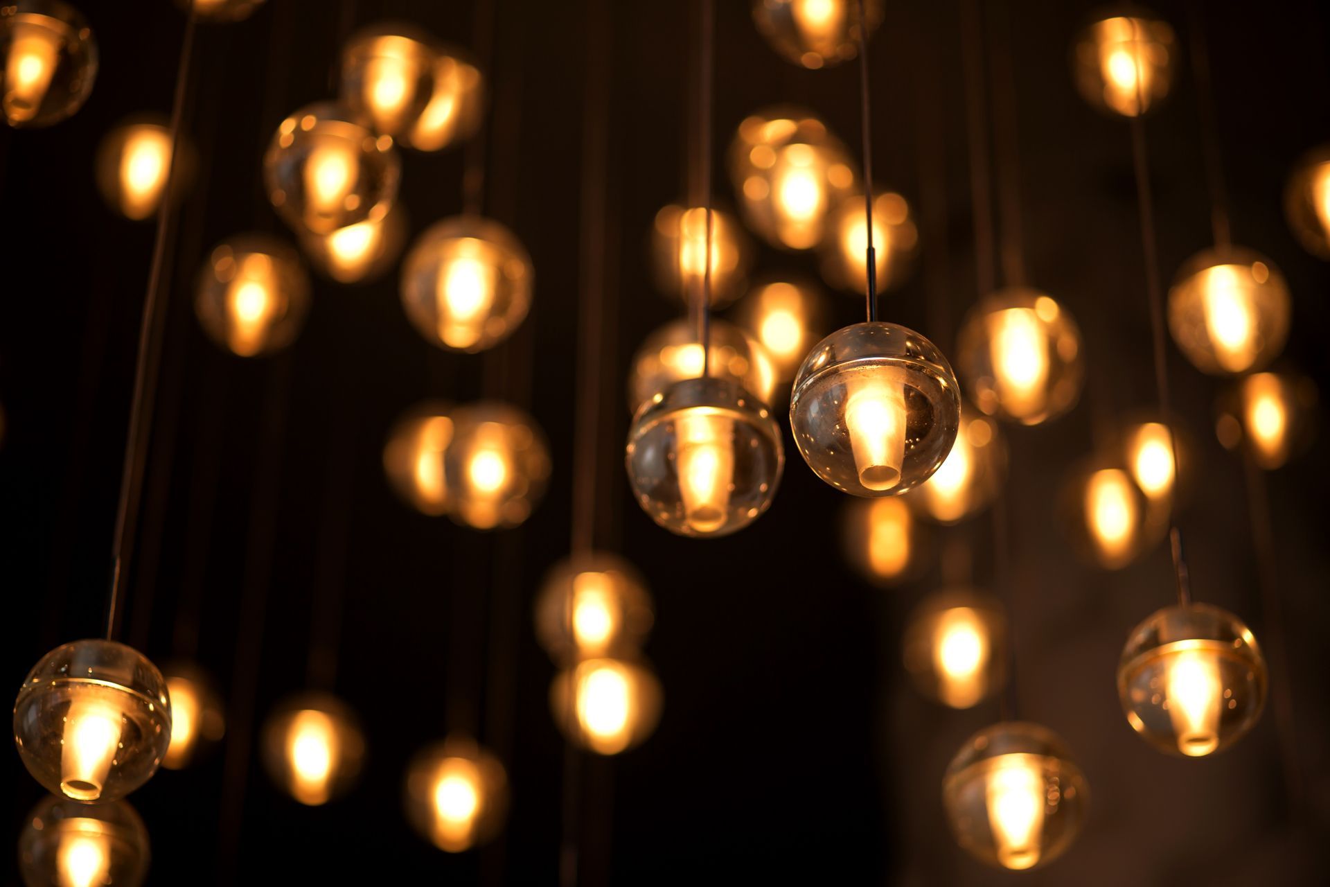 A close-up view of numerous glowing, spherical pendant lights hanging against a dark background.