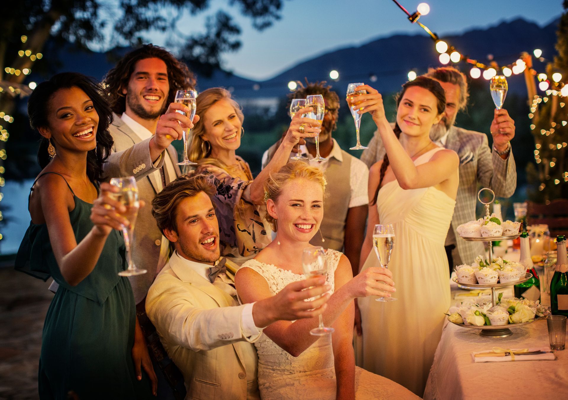 A group of friends in formal attire toast with champagne glasses at an outdoor evening event with string lights. A group of friends in formal attire toast with champagne glasses at an outdoor evening event with string lights.