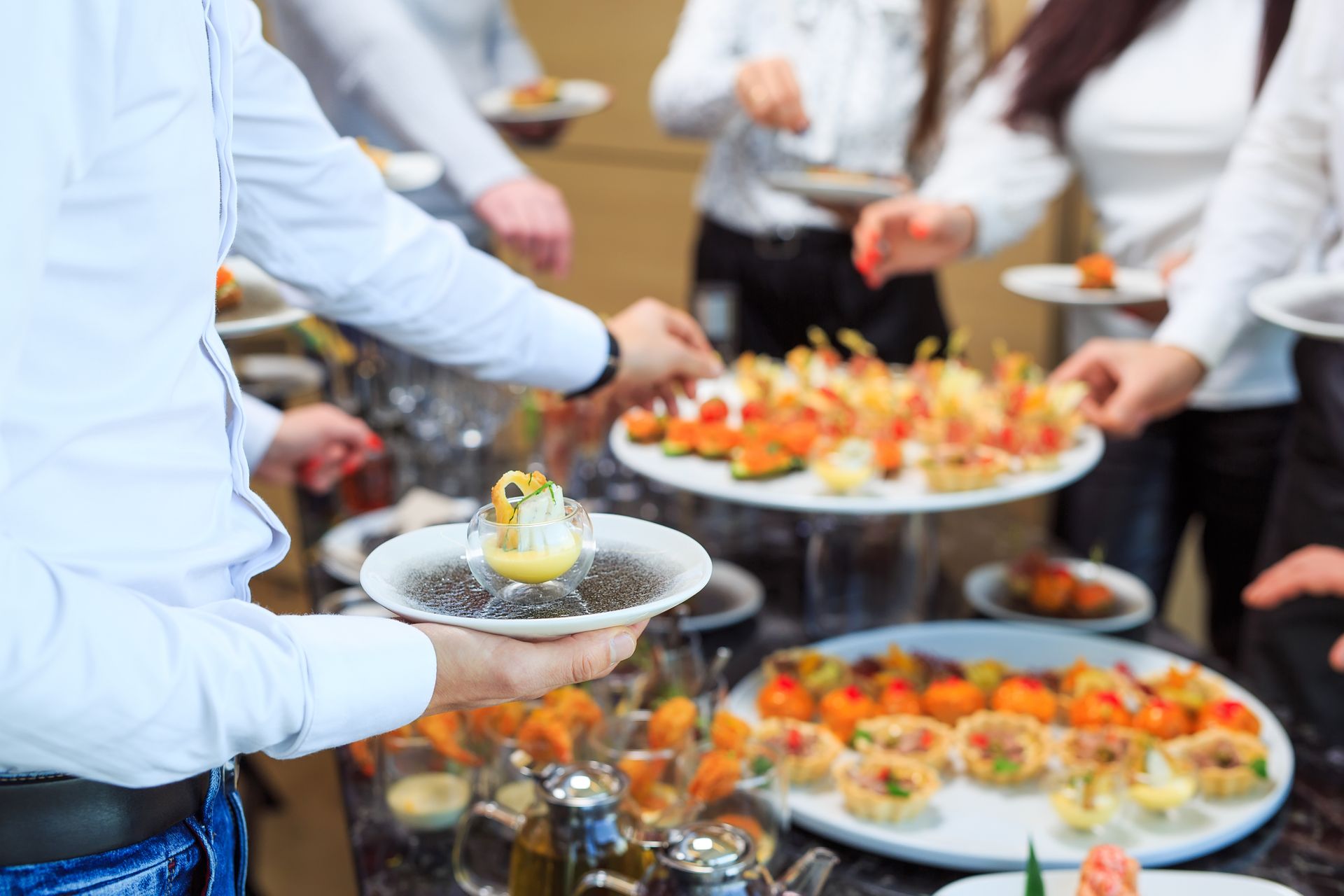 People serving appetizers at a catering buffet with trays of colorful finger foods People serving appetizers at a catering buffet with trays of colorful finger foods