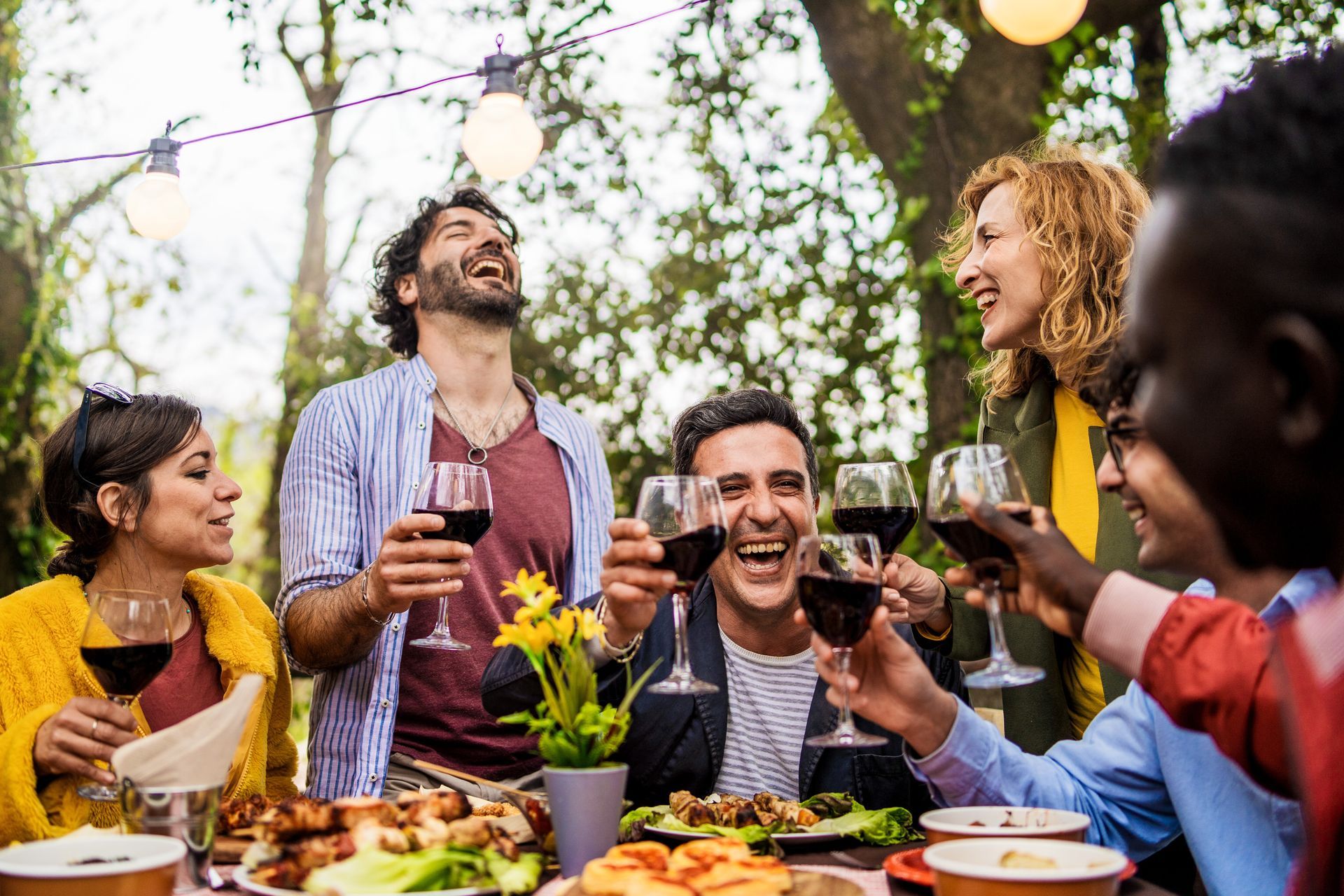 Friends toasting with wine at an outdoor dinner party under string lights Friends toasting with wine at an outdoor dinner party under string lights