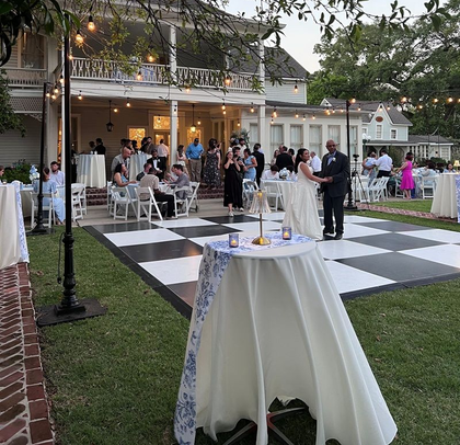 An outdoor wedding ceremony setup featuring white drapes, floral arrangements, chandeliers, and rows of white chairs.