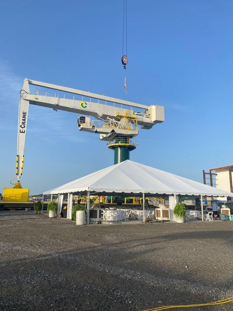 Large crane lifting equipment over a white tent at an industrial site under a blue sky.