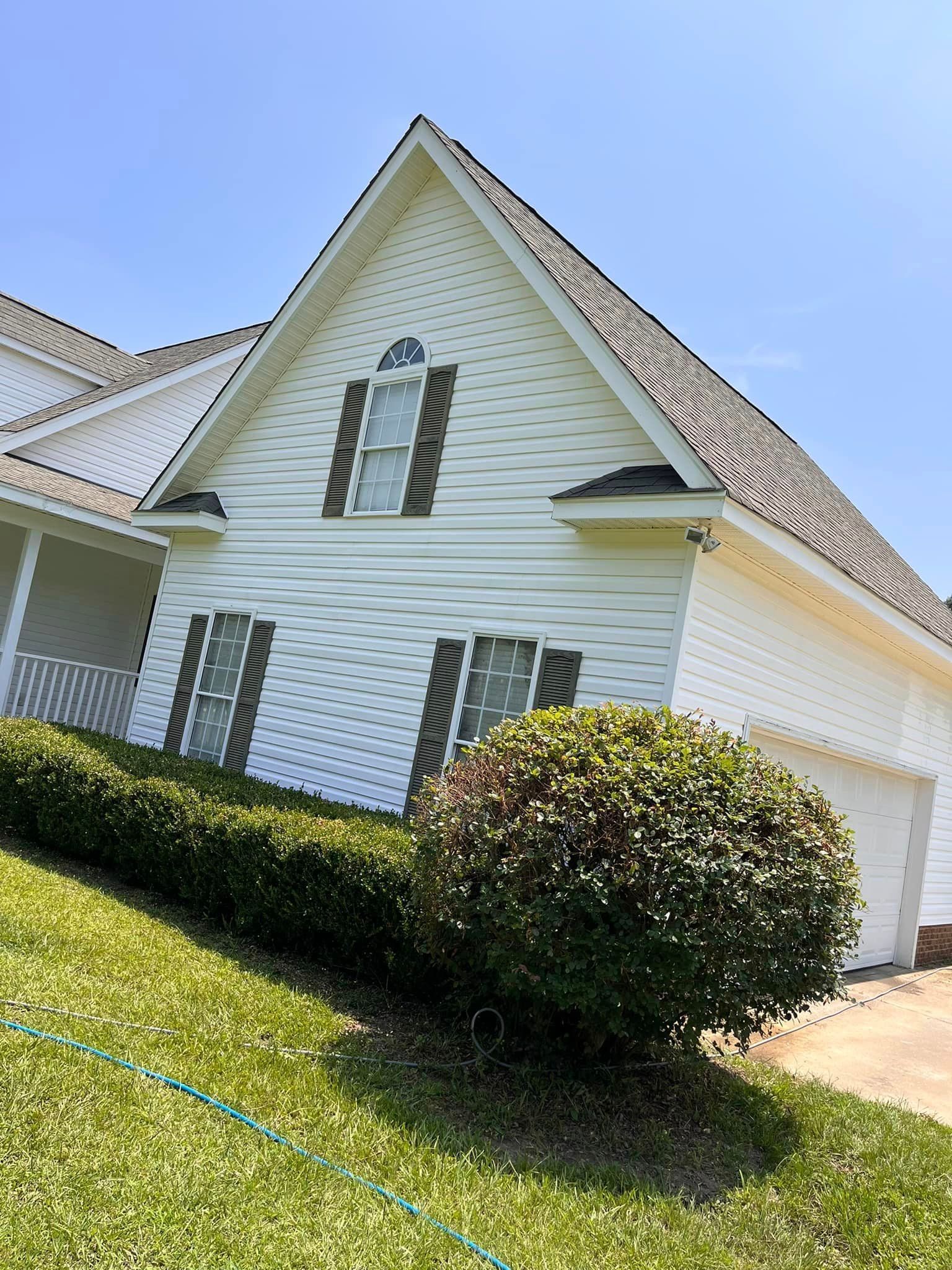 A white house with a brown roof and black shutters is sitting on top of a lush green hillside.