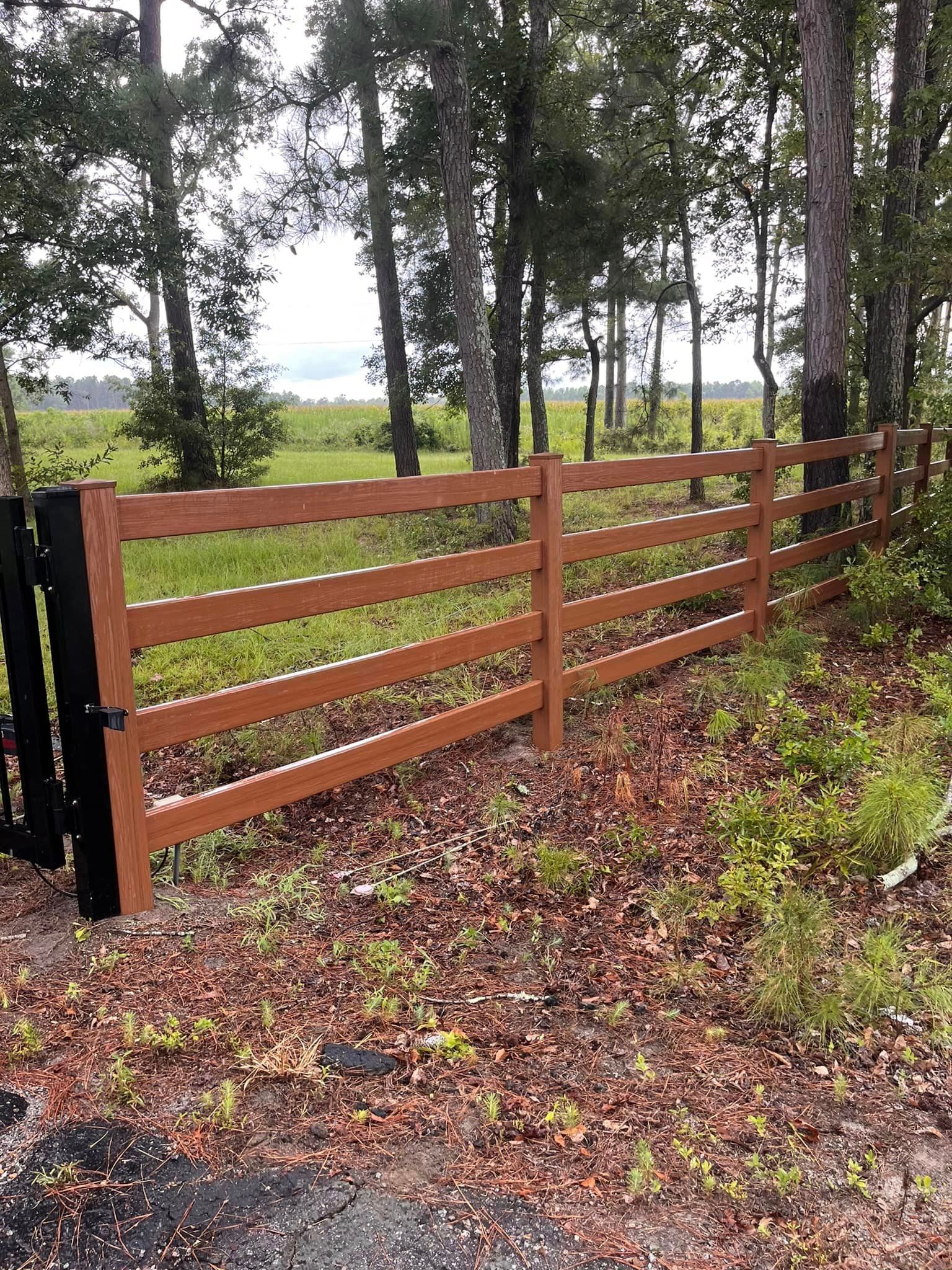 A wooden fence surrounds a field with trees in the background.