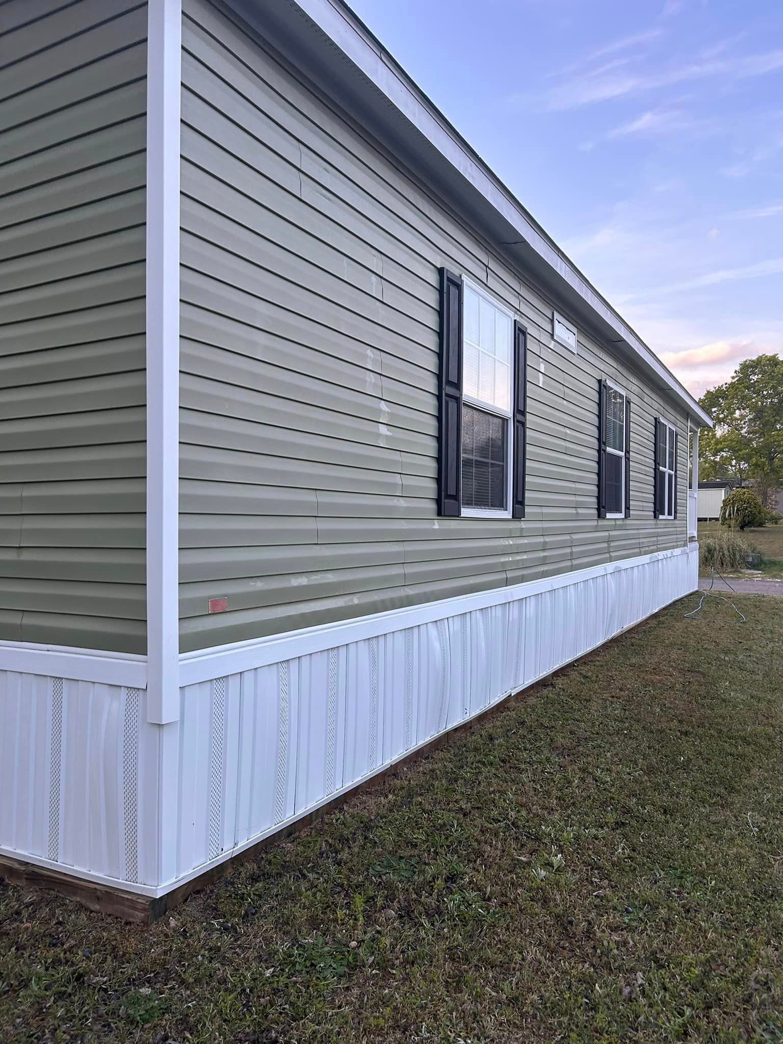 A mobile home with green siding and white trim is sitting on top of a lush green field.