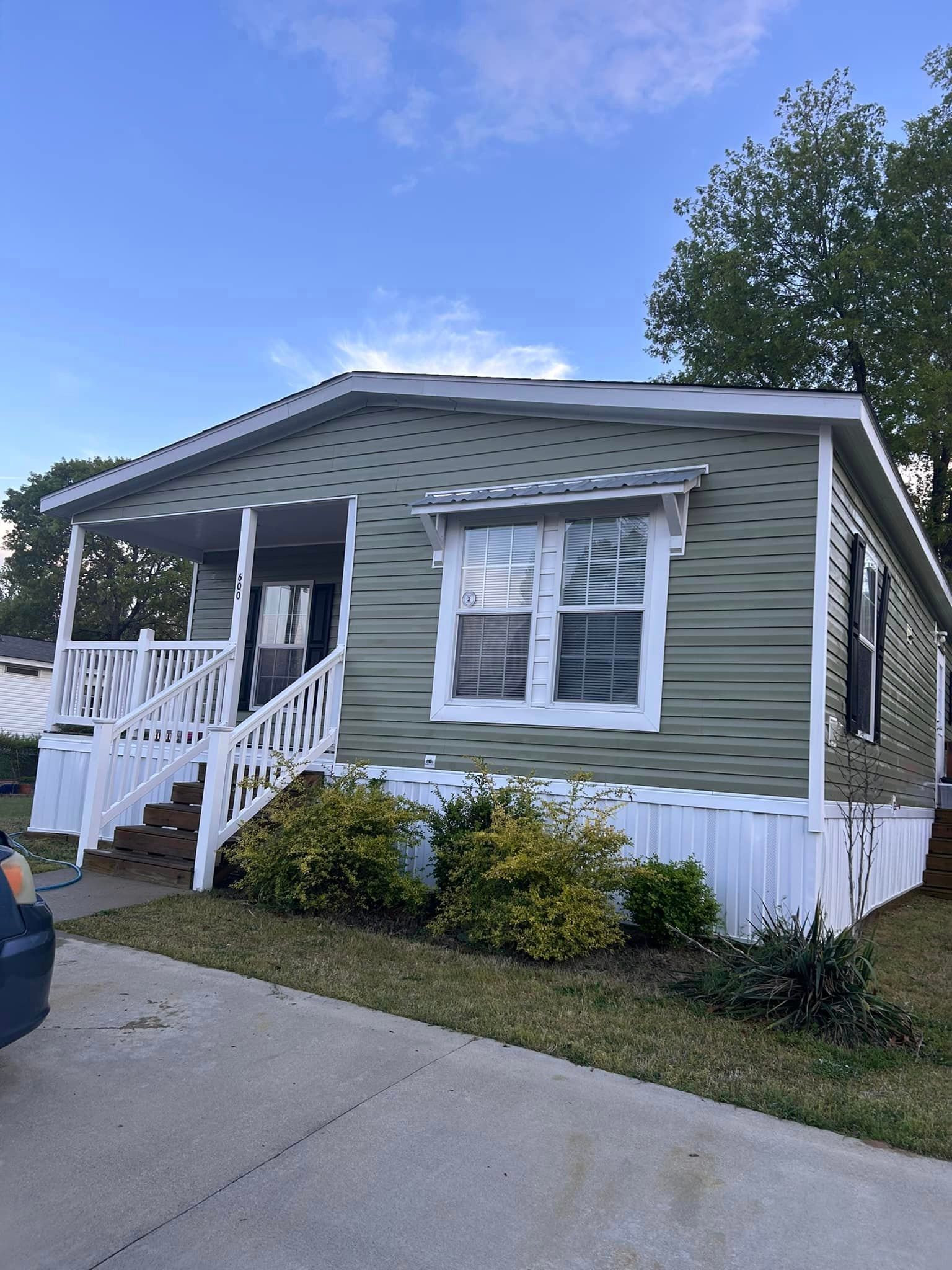 A green mobile home with a white porch and stairs.