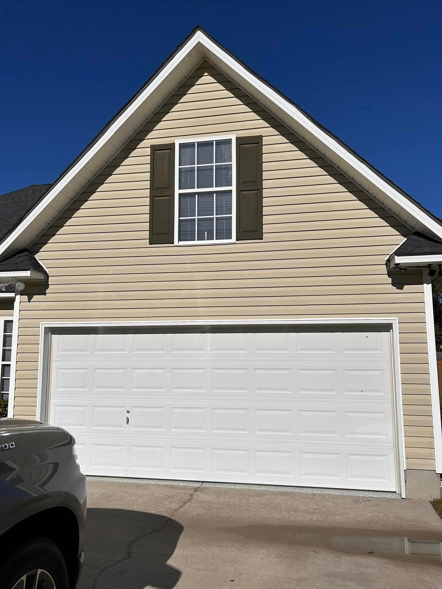 A car is parked in front of a house with a white garage door
