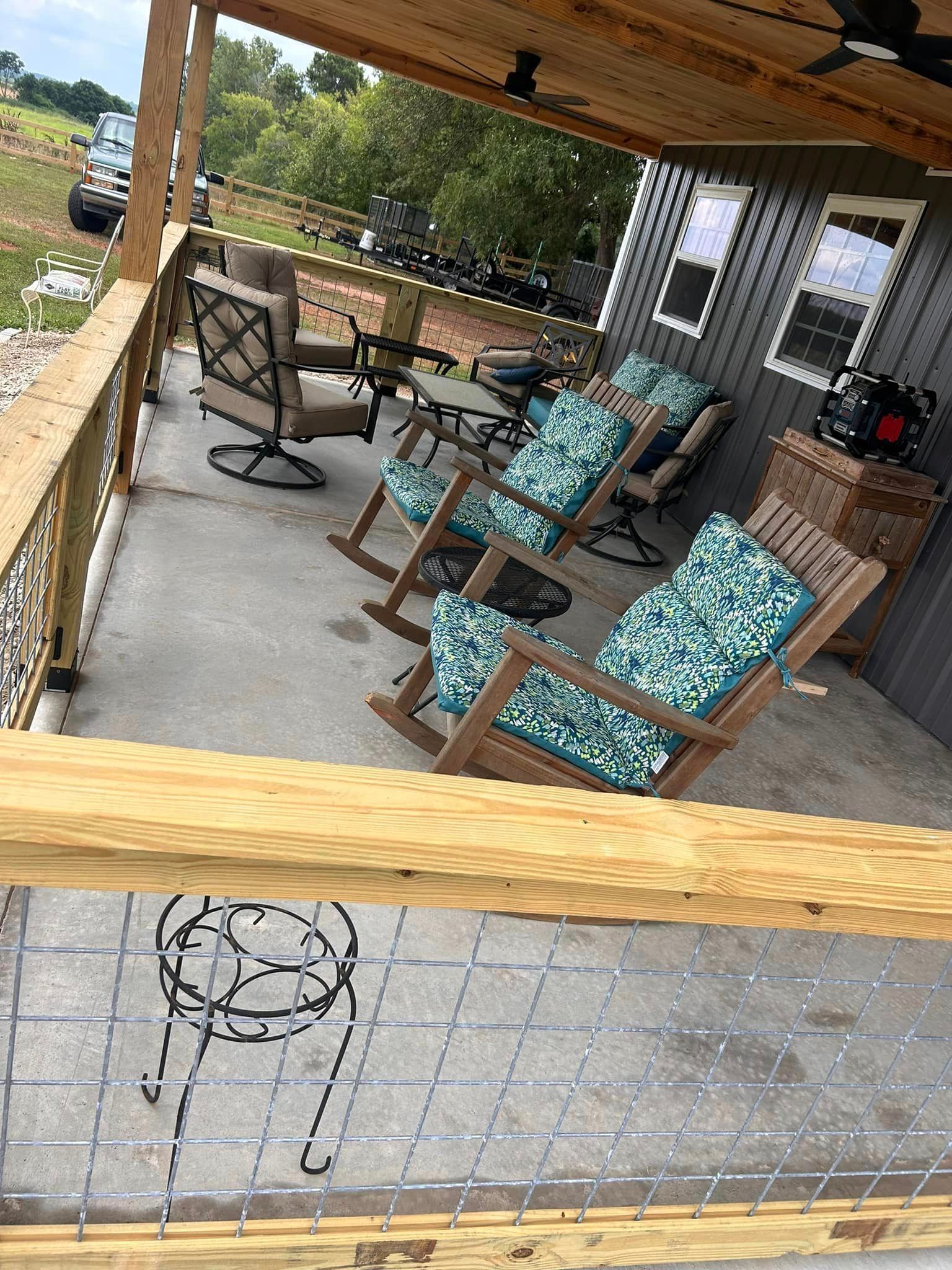 A porch with rocking chairs , tables , and a ceiling fan.