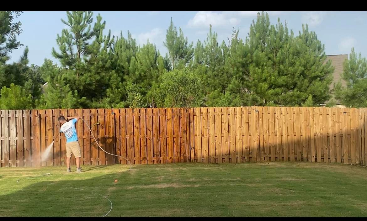 A man is cleaning a wooden fence with a pressure washer.