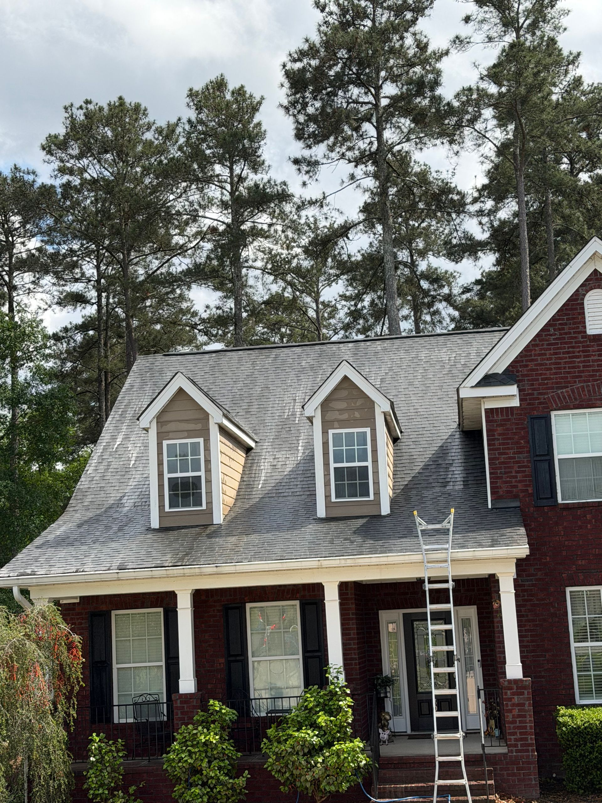 Brick house with gray shingled roof, two dormer windows, and a ladder leaning against the front porch.