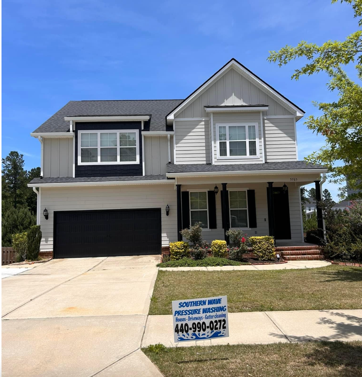 Two-story gray house with black garage door and a yard sign on a sunny day