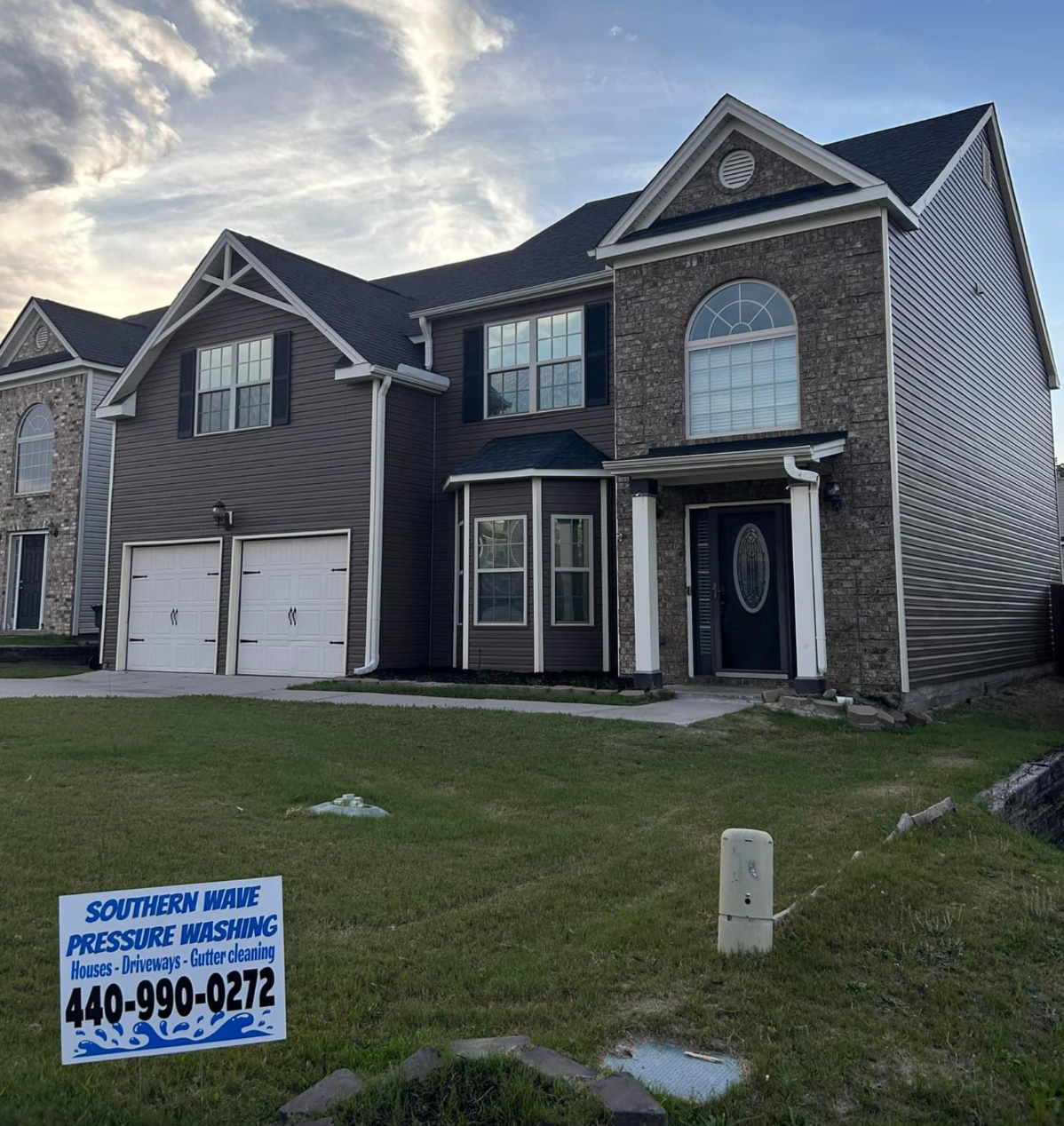 Two-story brick house with double garage and a yard sign for driveway pressure washing services