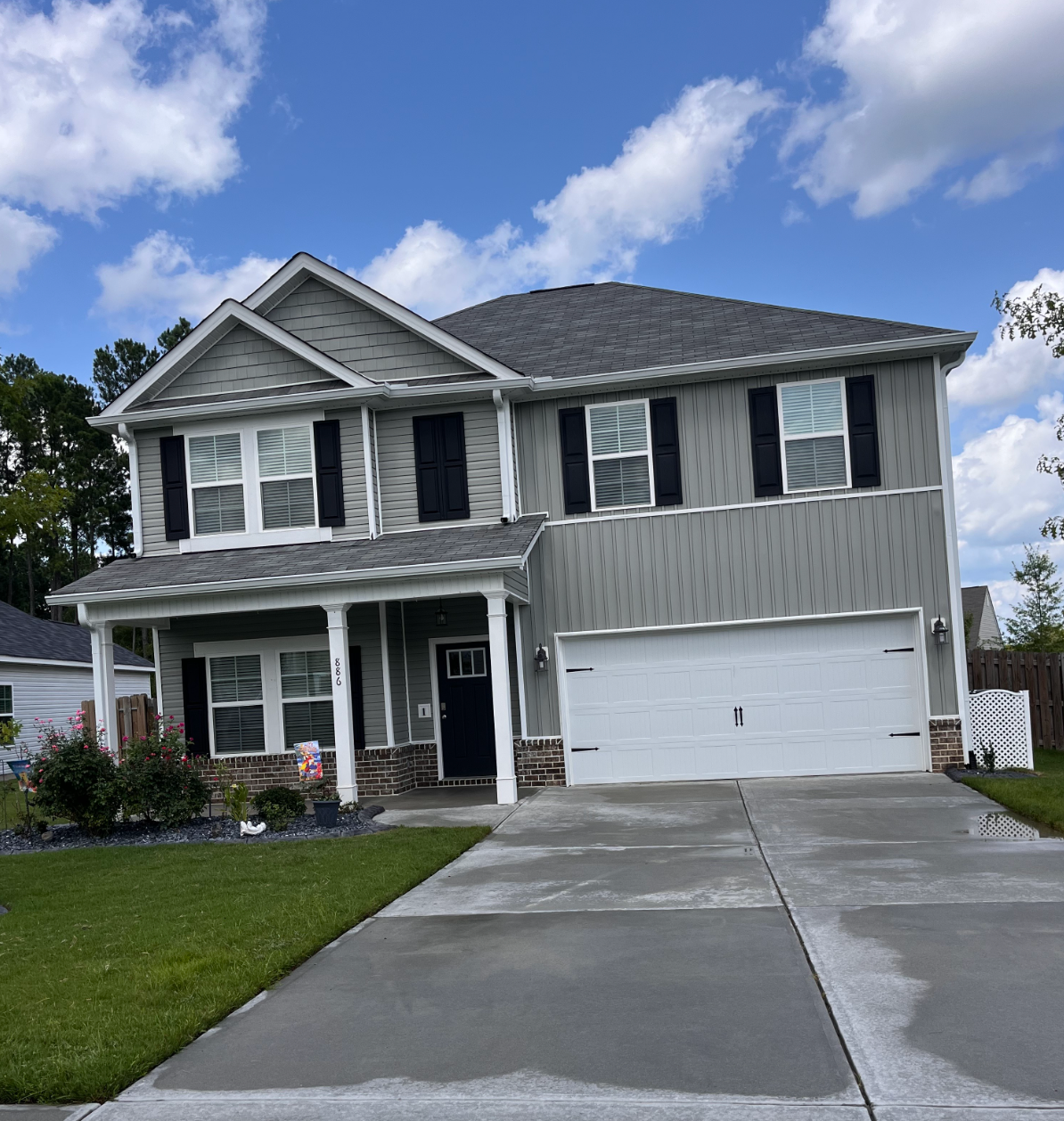 Two-story gray house with black shutters, white trim, and a double garage under a partly cloudy sky
