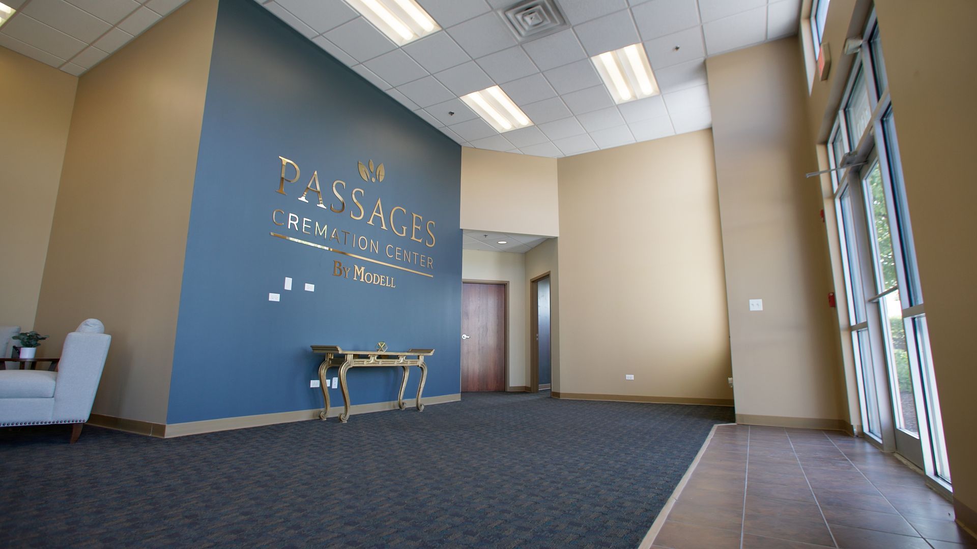 Empty lobby with blue accent wall, bench, tiled floor, and glass entrance doors on the right.