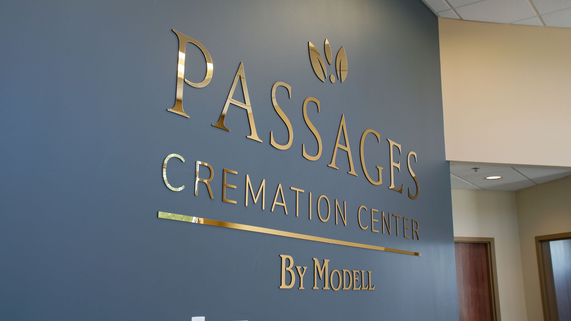 Gold “Passages Cremation Center” sign on a blue wall in a hallway