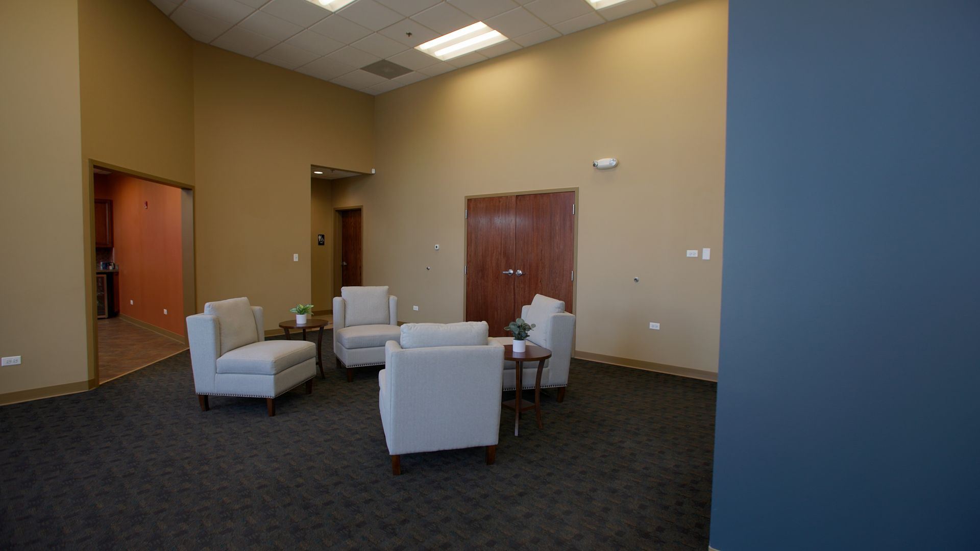 Modern lobby with white chairs, carpeted floor, wood doors, and beige walls.