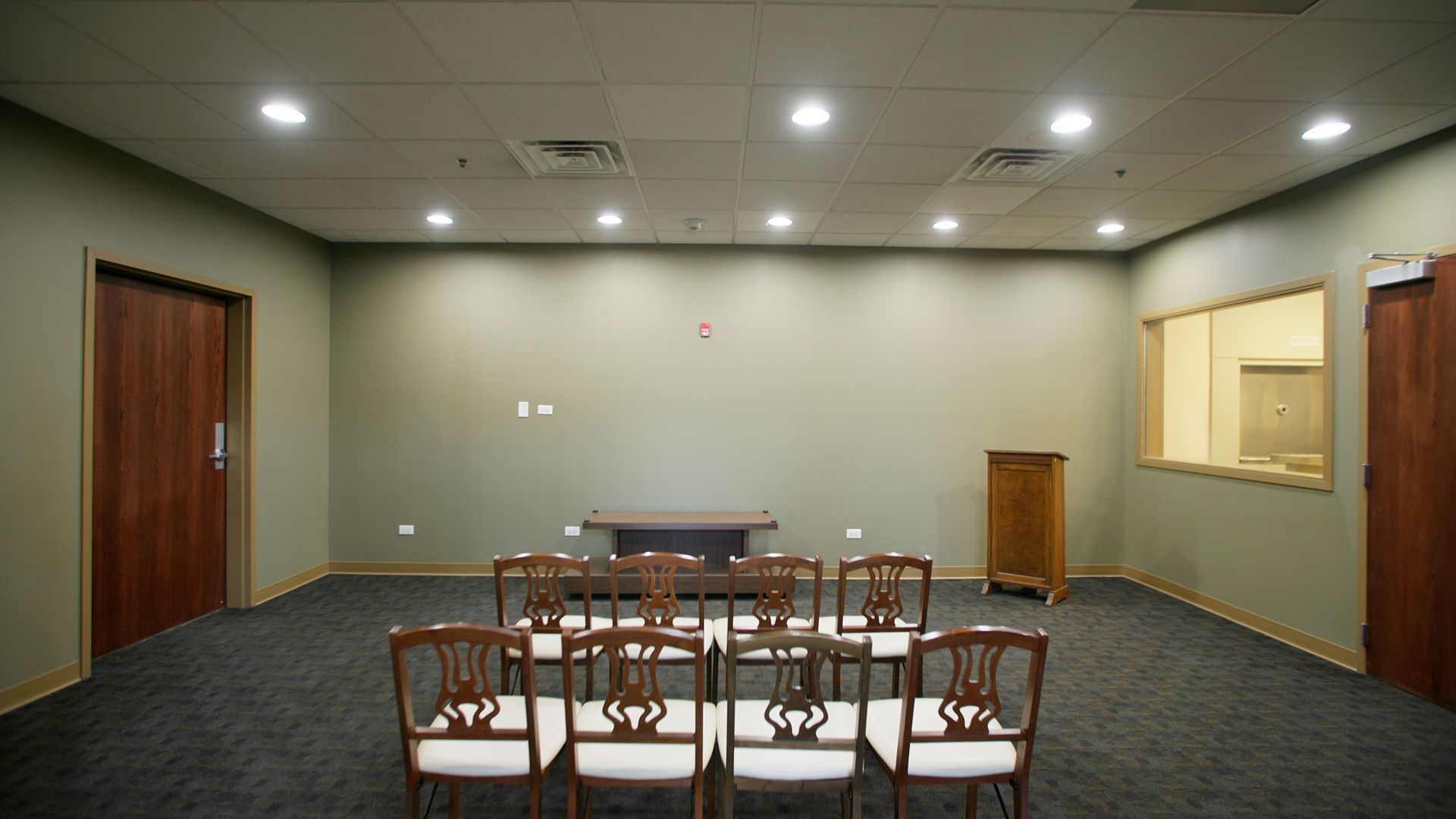 Conference room with rows of chairs, a table, and beige walls under recessed ceiling lights.