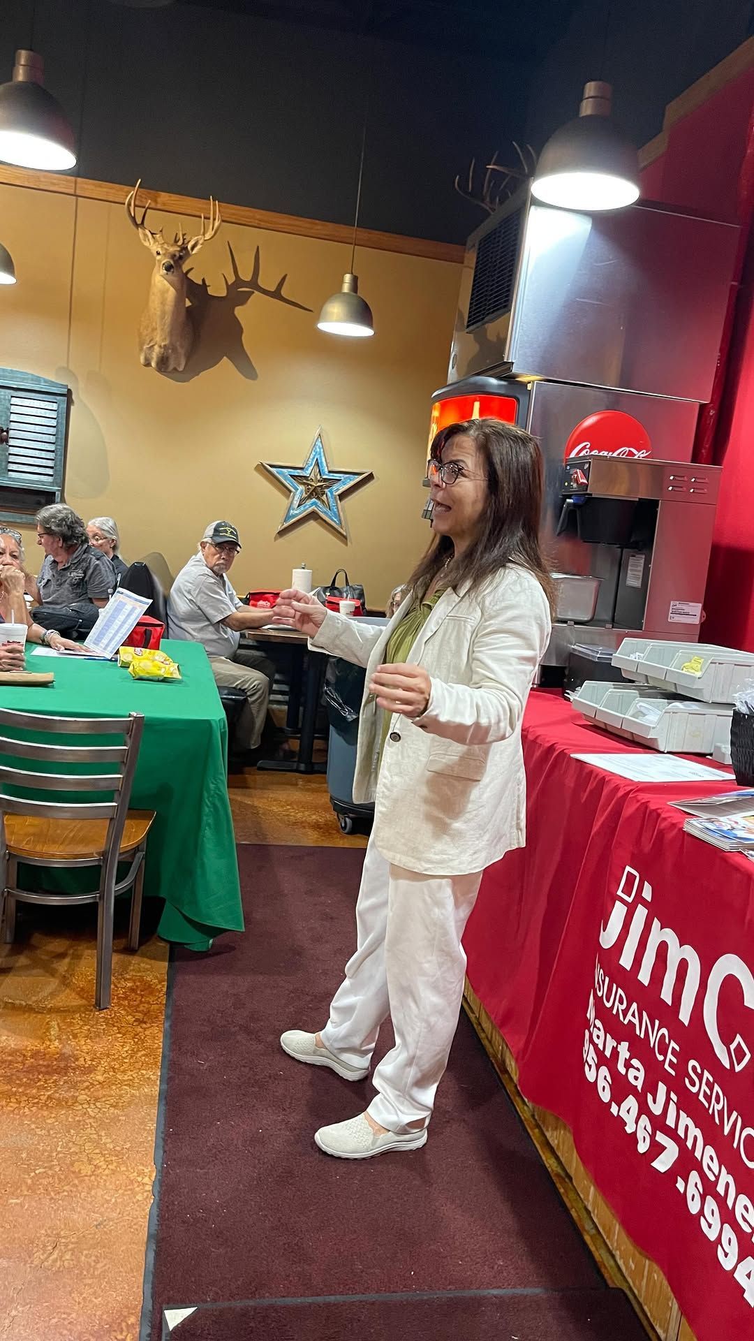 Woman standing in a festive restaurant beside a table with a green cloth and a red banner.