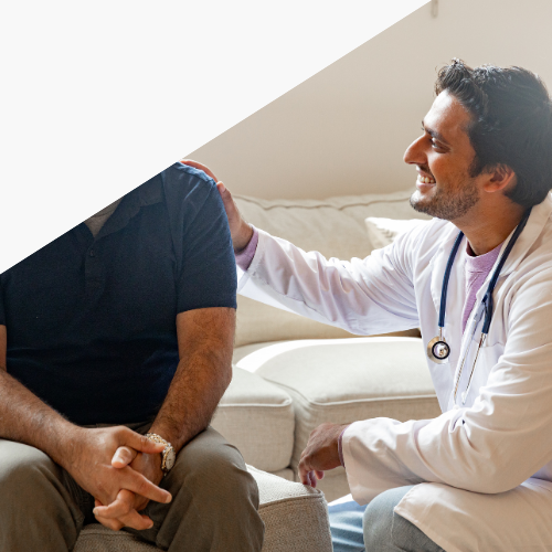 Doctor speaking with a seated patient in a bright living room, offering a reassuring touch