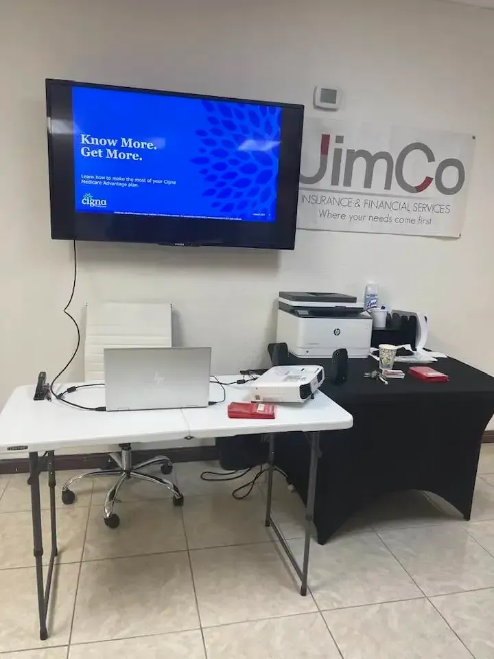 Trade show booth with TV, laptop, printer, and table under a JimCo banner.