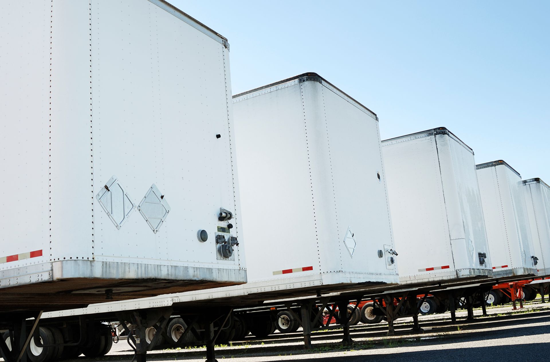 White semi-truck trailers parked in a row under a clear, blue sky.