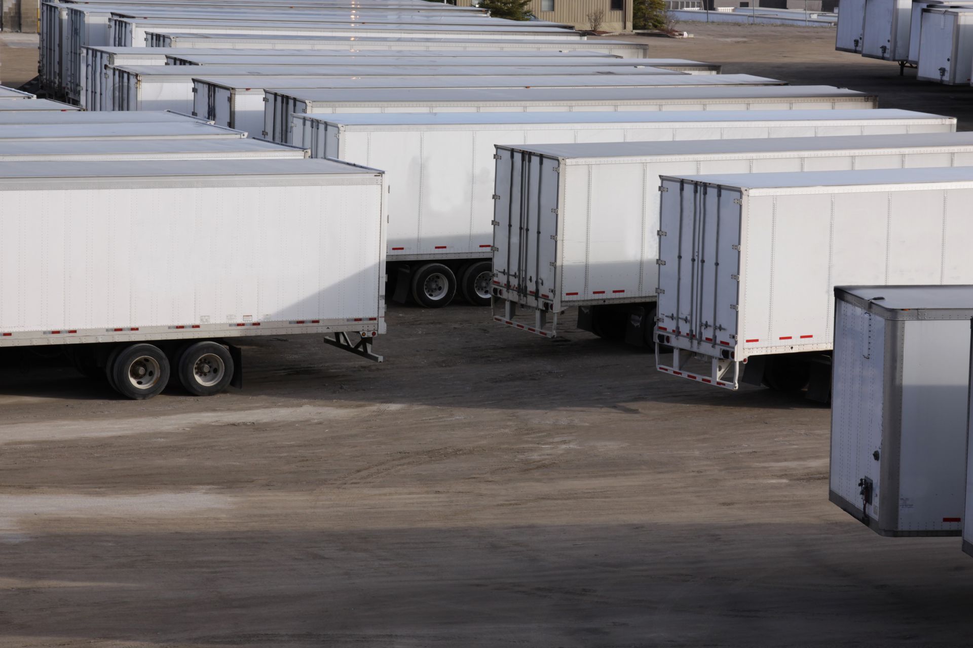 Rows of white semi-trailers parked in a dirt lot. Rows of white semi-trailers parked in a dirt lot.