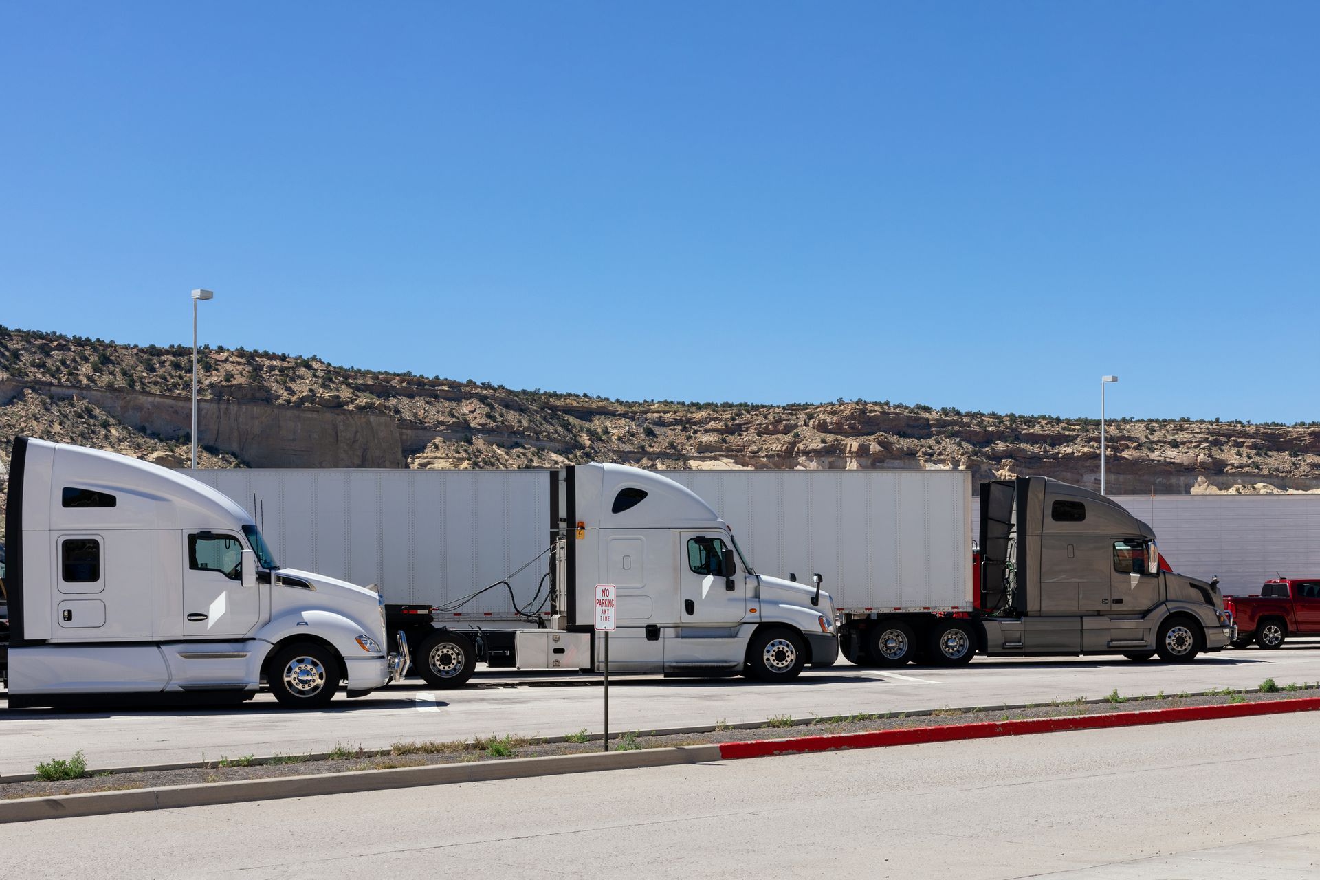 Three semi-trucks parked side by side in a rocky desert lot. Three semi-trucks parked side by side in a rocky desert lot.