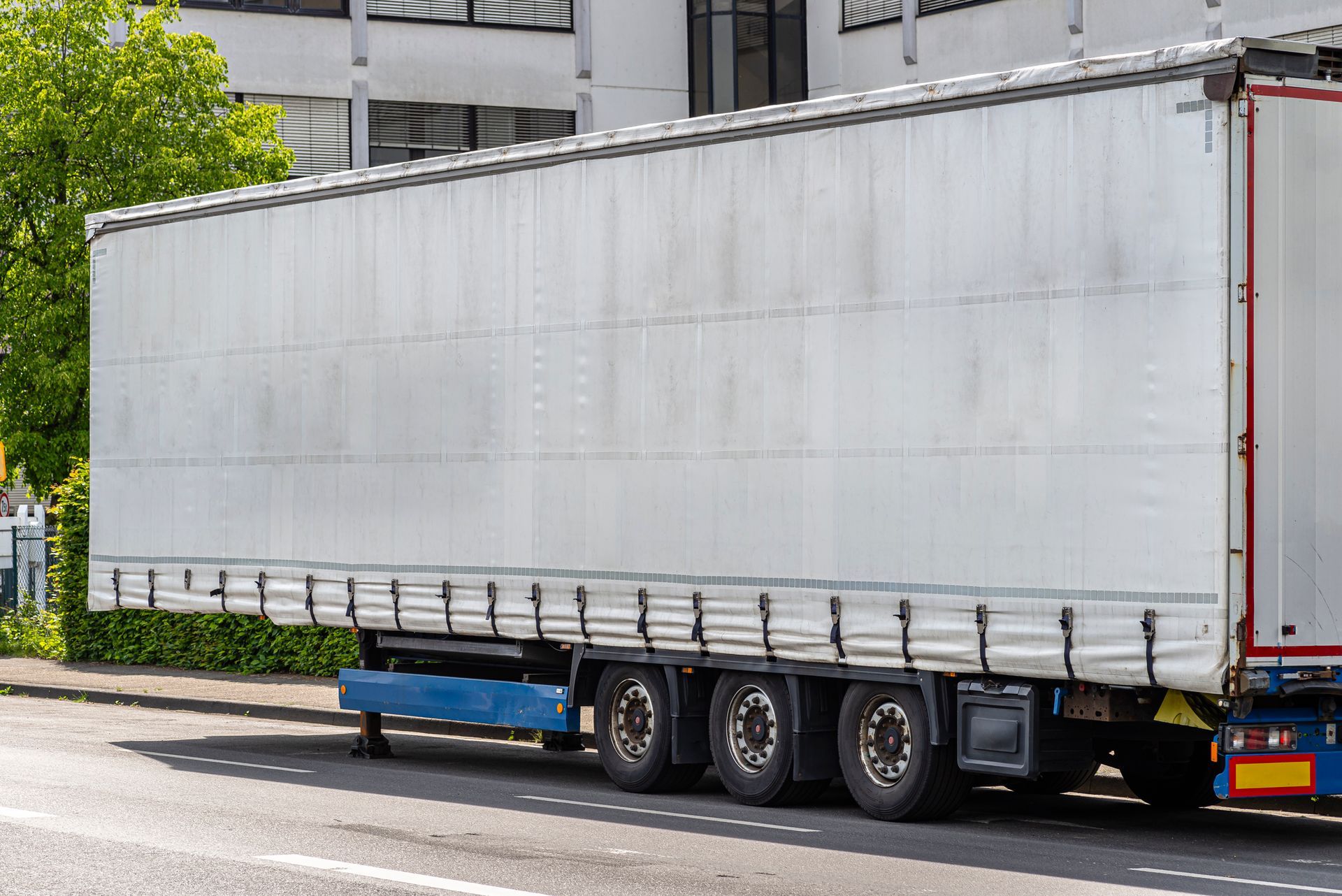A white semitrailer parked on the street provided by Ideal Leasing Services' trailer leasing in Ringgold, GA. Semi-trailer parked on a street with white canvas sides. Wheels and blue undercarriage are visible.