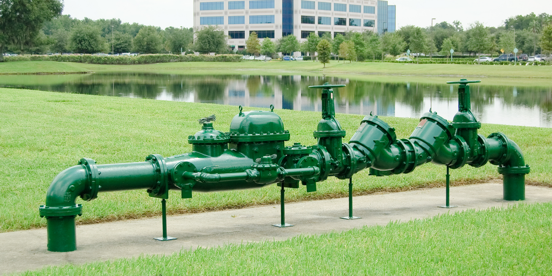 A row of green pipes in a park with a building in the background